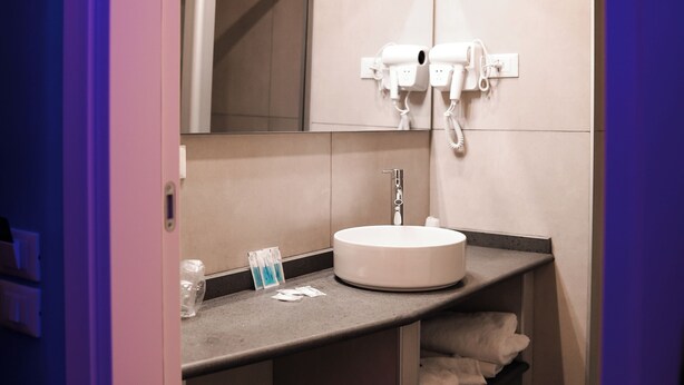 A modern bathroom with a round sink, a mirror, and a hairdryer mounted on the wall. - Hotel Miravalle (Naples)
