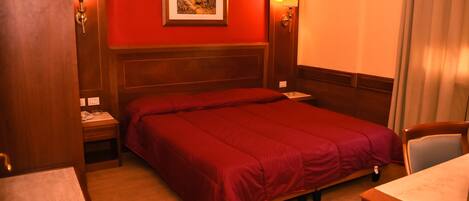A hotel room with a large bed, wooden headboard, two bedside tables, a nightstand, and a framed picture on the wall.