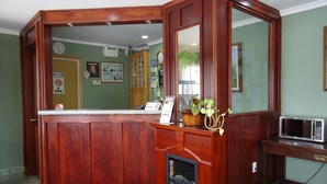 Un espace d’accueil comprenant un comptoir de réception en bois, une cheminée, un miroir et un four à micro-ondes.