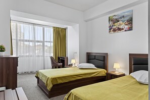 A hotel room with two beds, a desk, a chair, a window with curtains, a painting on the wall, and a lamp on the nightstand. - Lina Hotel (Bucharest)