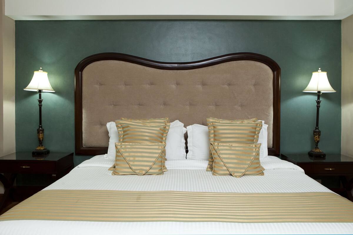 A neatly made bed with striped bedding, a tufted headboard, and two bedside lamps on matching nightstands.