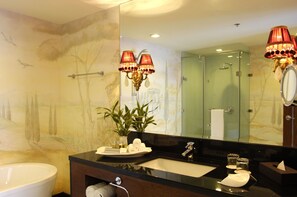A bathroom with a large mirror, a sink, a bathtub, and a shower. There are two wall-mounted lamps and a potted plant on the counter. - Hotel Celeste (Makati)