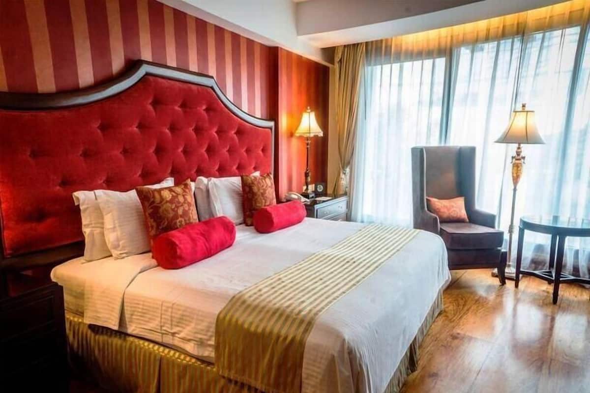 A hotel room with a large bed, a chair, a nightstand, and a lamp.