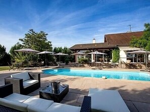 Piscina com espreguiçadeiras e guarda-sóis, cercada por um espaço de lazer ao ar livre com mobiliário.