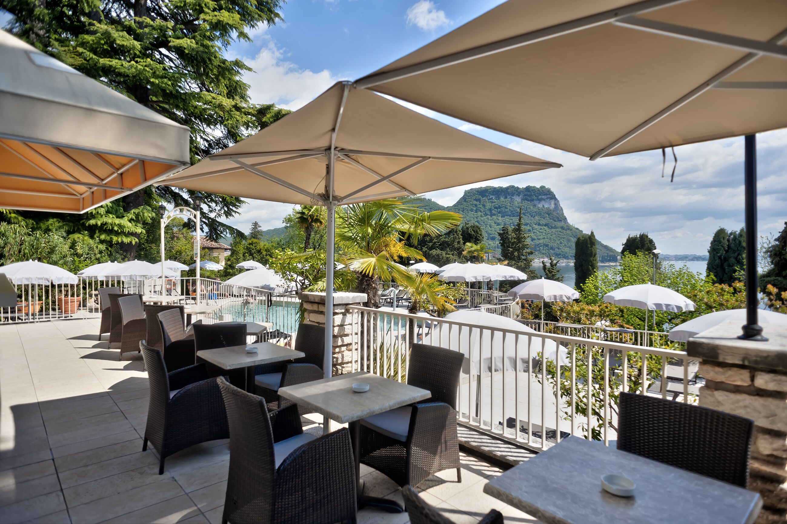 An outdoor seating area with tables and chairs, umbrellas, and a view of a mountainous landscape.