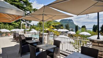An outdoor seating area with tables and chairs, umbrellas, and a view of a mountainous landscape.