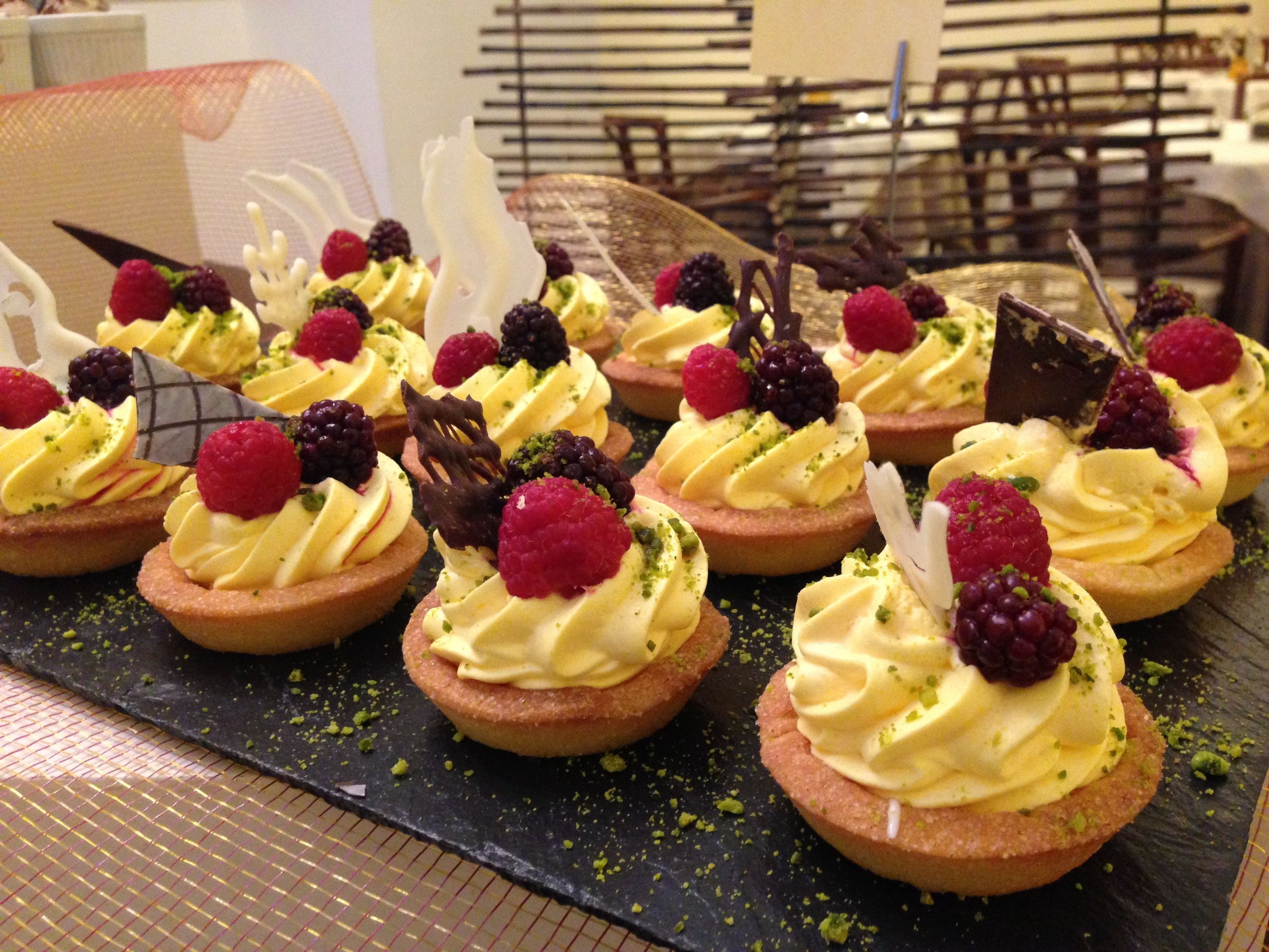 Un présentoir de desserts avec plusieurs tartelettes garnies de crème fouettée et de fruits rouges.
