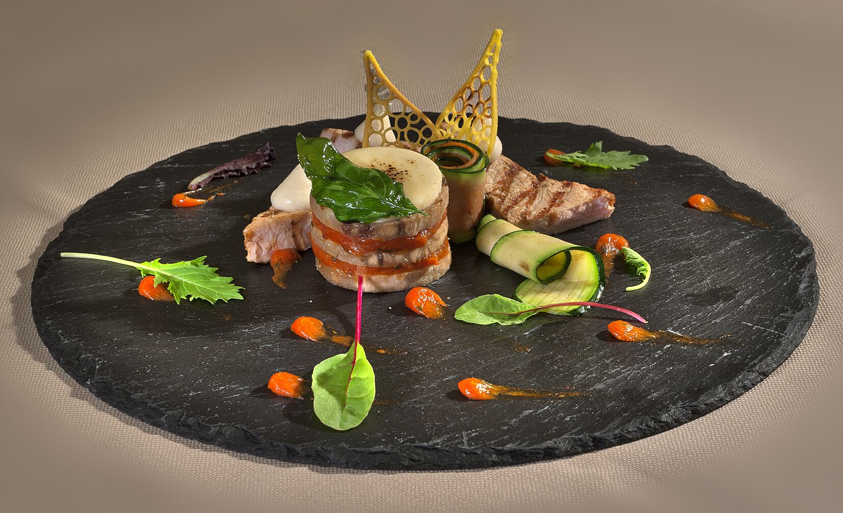 Eine schwarze Schieferplatte mit verschiedenen Lebensmitteln, darunter geschnittenes Fleisch, Gemüse und Garnituren.
