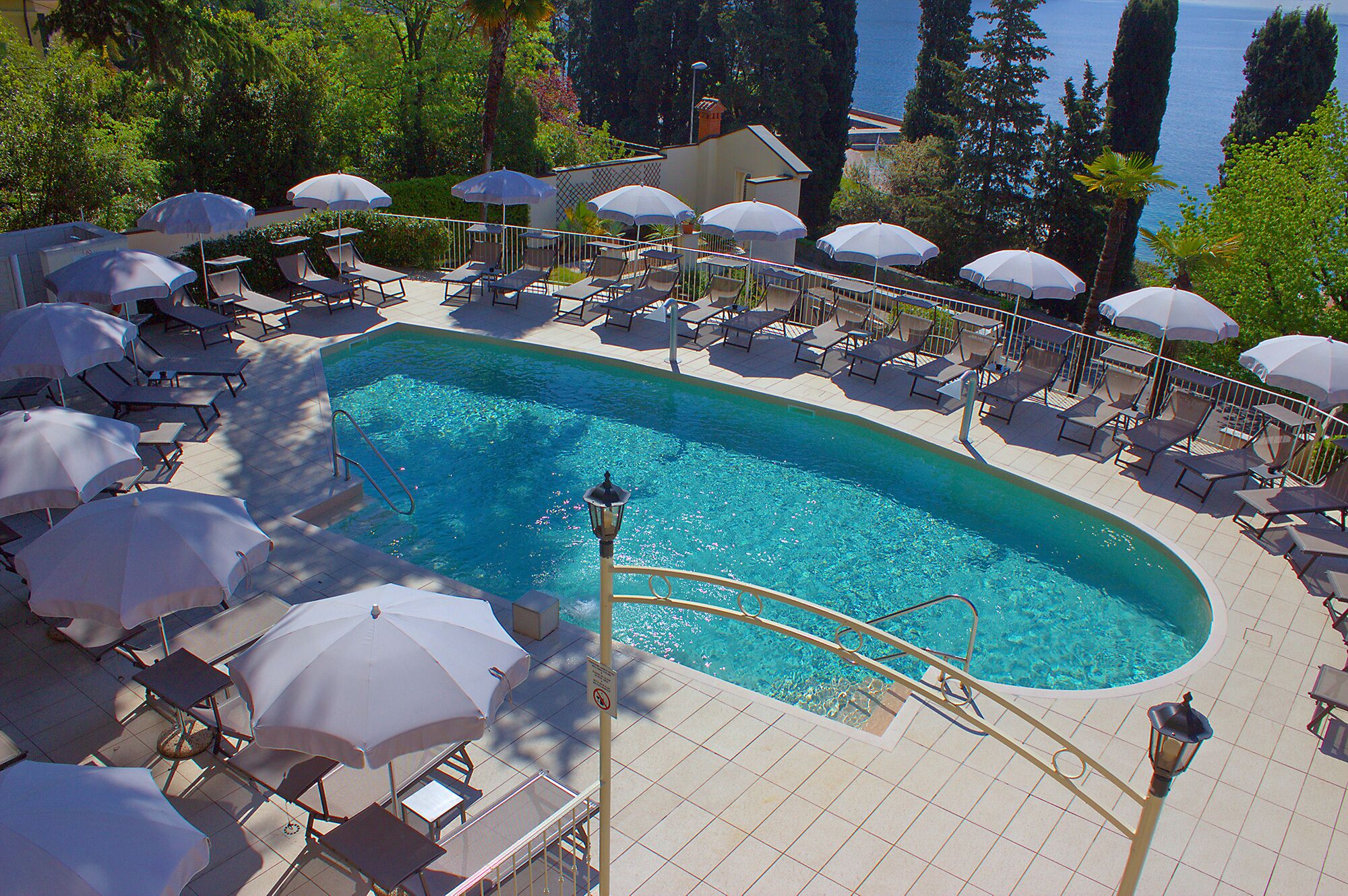 A poolside area with sun loungers and umbrellas, a clear pool, and a view of the sea.
