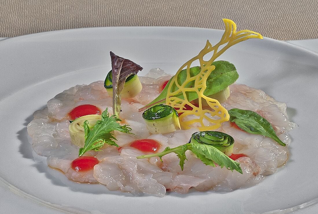 Un plato blanco con mariscos, adornado con hojas verdes y toques rojos.