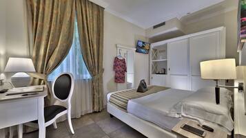 A hotel room with a bed, desk, chair, TV, wardrobe, and a lamp.