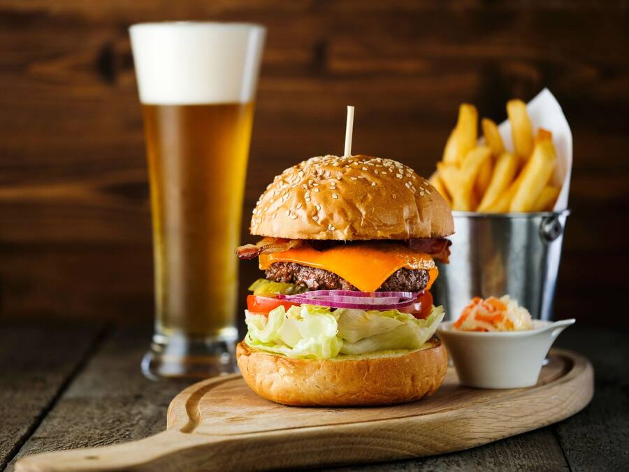 Una hamburguesa con papas fritas y una cerveza sobre una mesa de madera.