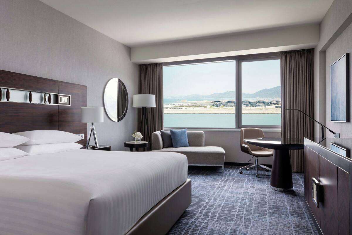 Ein modernes Hotelzimmer mit einem großen Bett, einer Couch, einem Schreibtisch und Blick auf ein Gewässer sowie Berge.