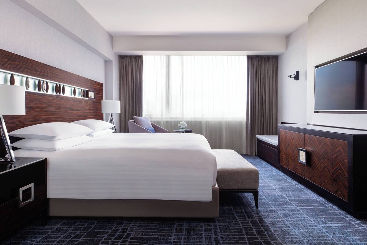 Ein Hotelzimmer mit einem großen Bett, einem Fernseher, einem Schreibtisch und einem Fenster mit Vorhängen.