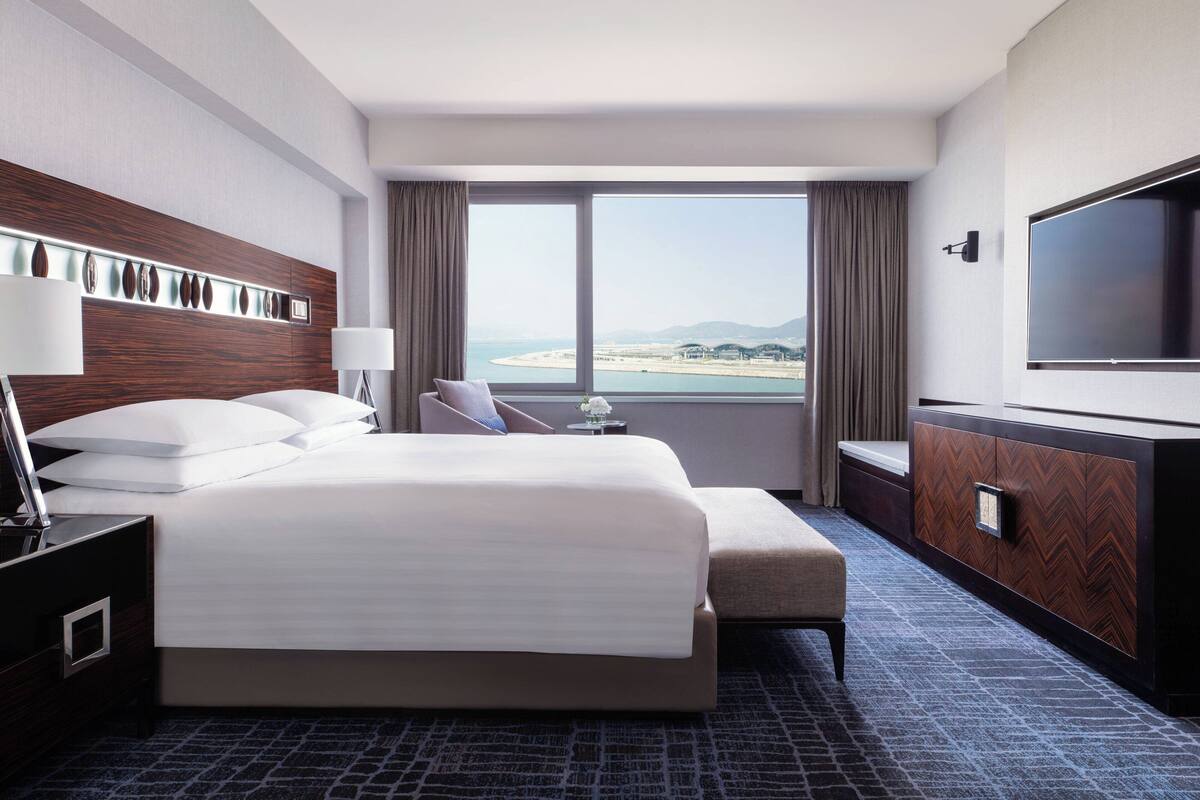 Ein Hotelzimmer mit einem großen Bett, einem Fernseher, einem Schreibtisch und Blick auf den Strand.