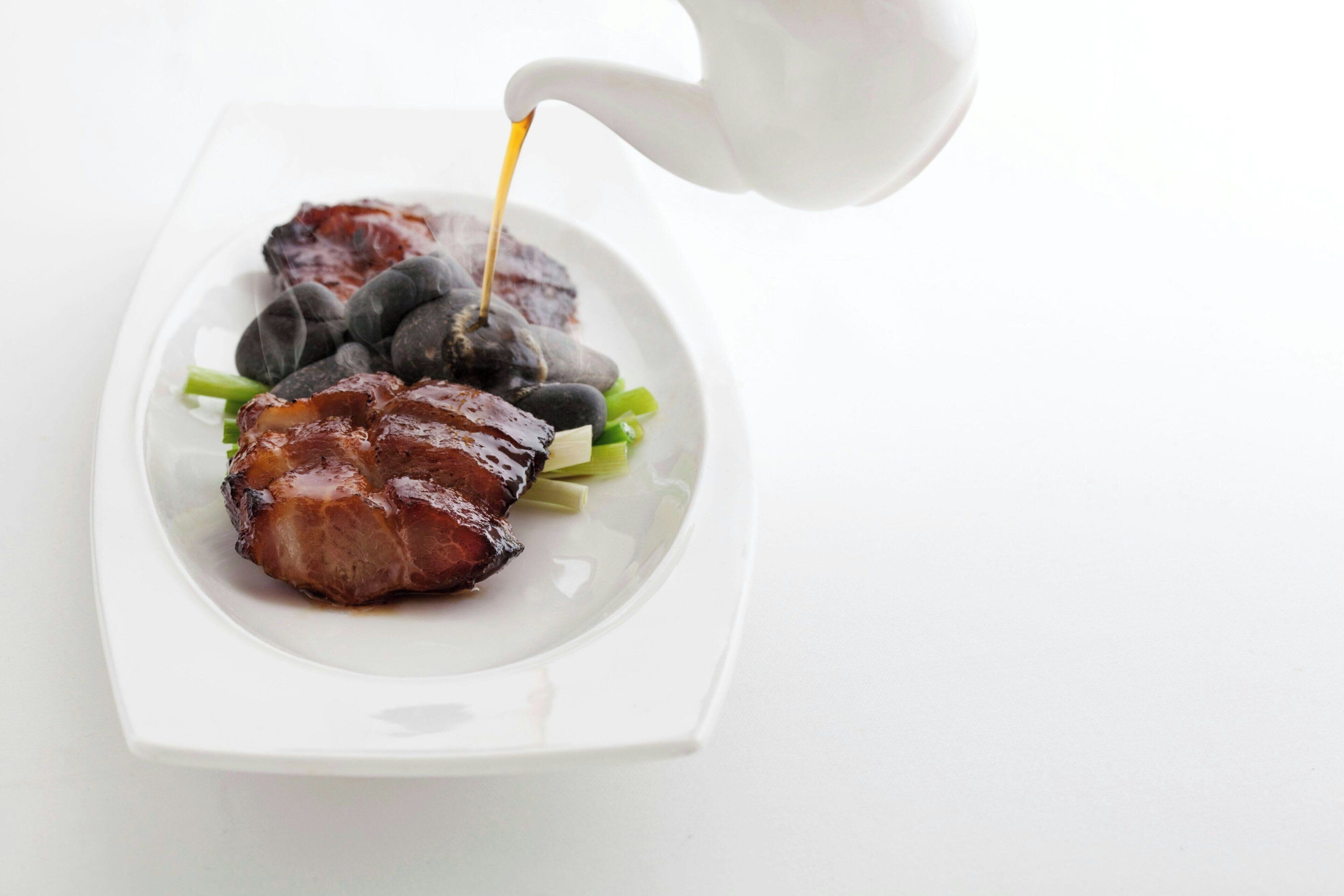 Une assiette blanche avec un morceau de viande, des objets ronds noirs et une garniture verte.