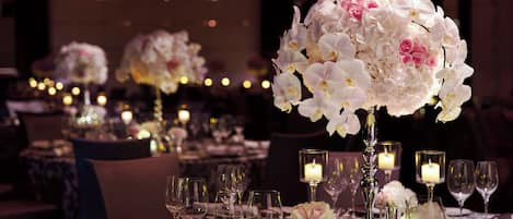 A dining table set with glassware, plates, and a centerpiece of white flowers.