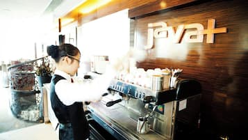 Una máquina de café con un respiradero de vapor, una persona con delantal blanco y un letrero con la palabra 'Javat' en la pared.