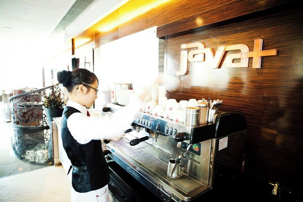 Una máquina de café con un respiradero de vapor, una persona con delantal blanco y un letrero con la palabra 'Javat' en la pared.