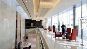 Un hall d’hôtel moderne avec une rambarde en verre, un espace salon et un comptoir d’accueil.