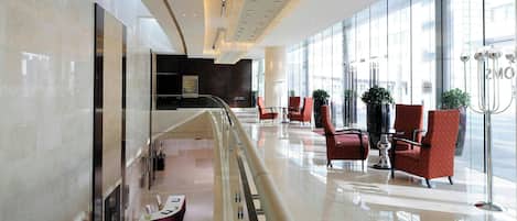 Un hall d’hôtel moderne avec une rambarde en verre, un espace salon et un comptoir d’accueil.