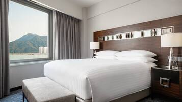 A hotel room with a large bed, a nightstand, a lamp, and a view of mountains through a window.