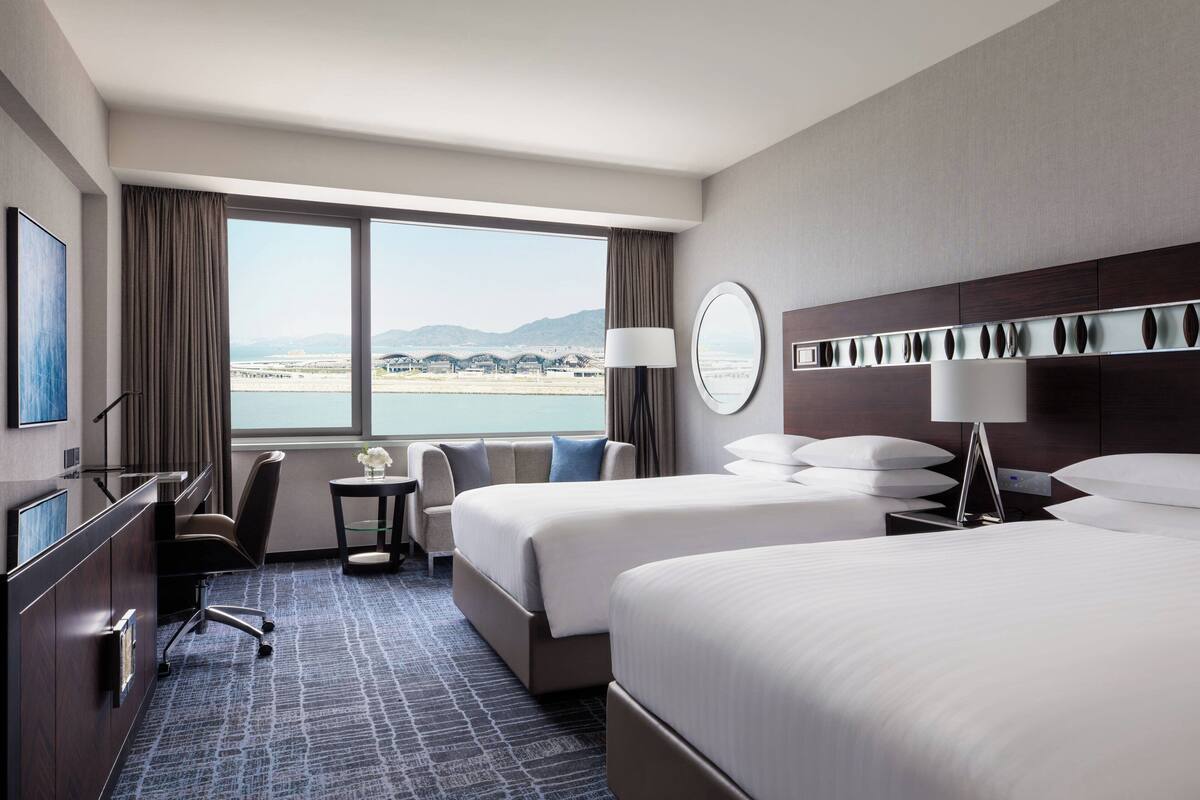Ein Hotelzimmer mit zwei Betten, einem Schreibtisch, einem Stuhl, einer Lampe und Meerblick.