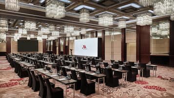 A conference room with rows of tables and chairs, a large screen, and chandeliers.