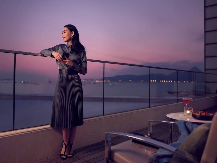Eine Frau steht auf einem Balkon mit Blick auf eine Stadtlandschaft im Abenddämmerung.