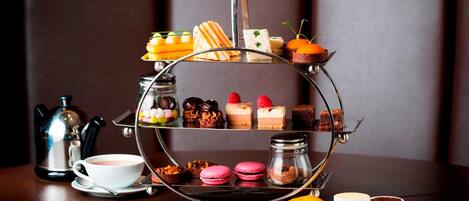 A three-tiered dessert stand with various pastries and desserts, a coffee cup, and a teapot on a table.