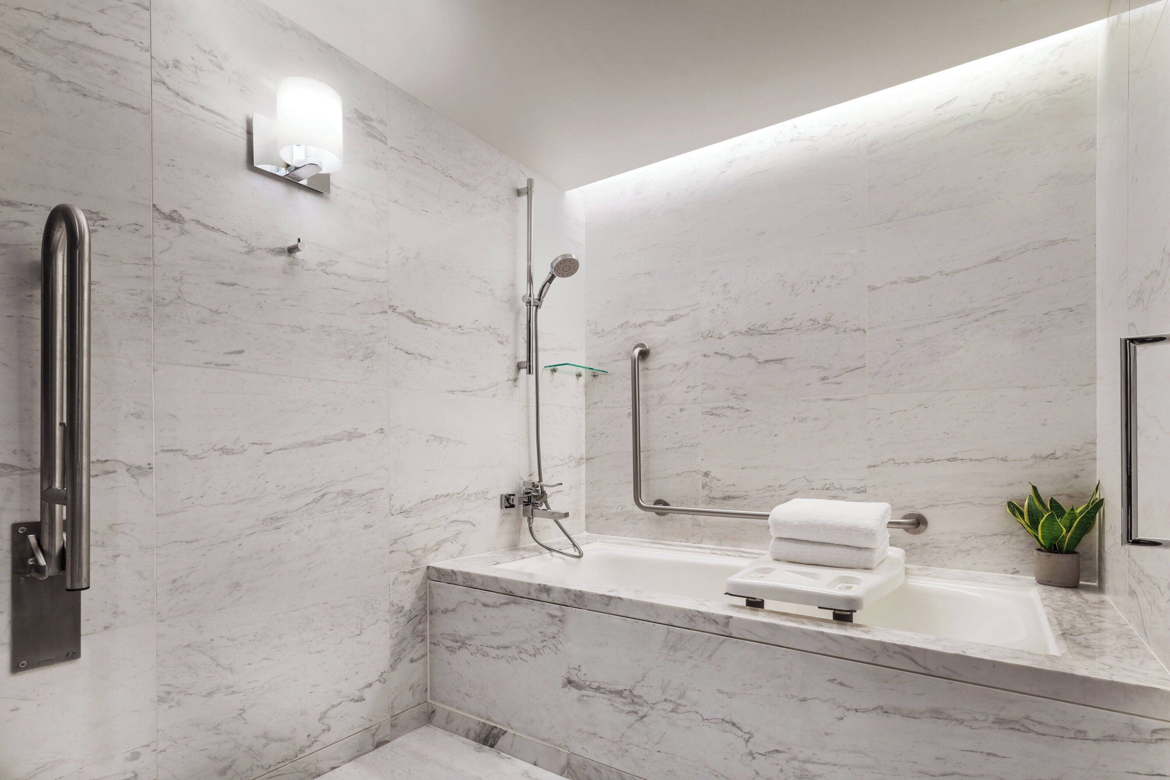 A modern bathroom with a marble wall, a built-in shower, a glass-enclosed bathtub, and a small potted plant.
