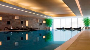 Une piscine intérieure moderne, dotée de plusieurs couloirs de nage, d’un éclairage intégré et d’une grande fenêtre laissant entrer la lumière naturelle.
