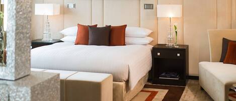 Una habitación de hotel con una cama grande, dos mesitas de noche con lámparas, una mesita pequeña con un florero y un sofá.