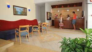 A reception area with a wooden reception desk, a red sofa, and a dining area with wooden chairs. - Petrosana Hotel Apartments (Ayia Napa)