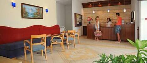 A reception area with a wooden reception desk, a red sofa, and a dining area with wooden chairs.