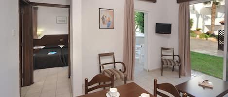A hotel room with a bed, a dining table with chairs, a TV, and a view of the outside.