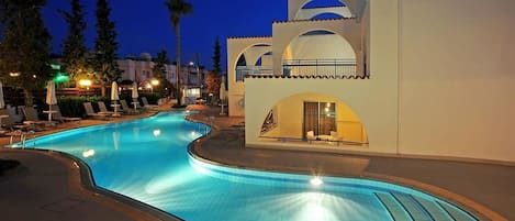A swimming pool with lounge chairs and umbrellas, surrounded by buildings with arched windows and balconies.