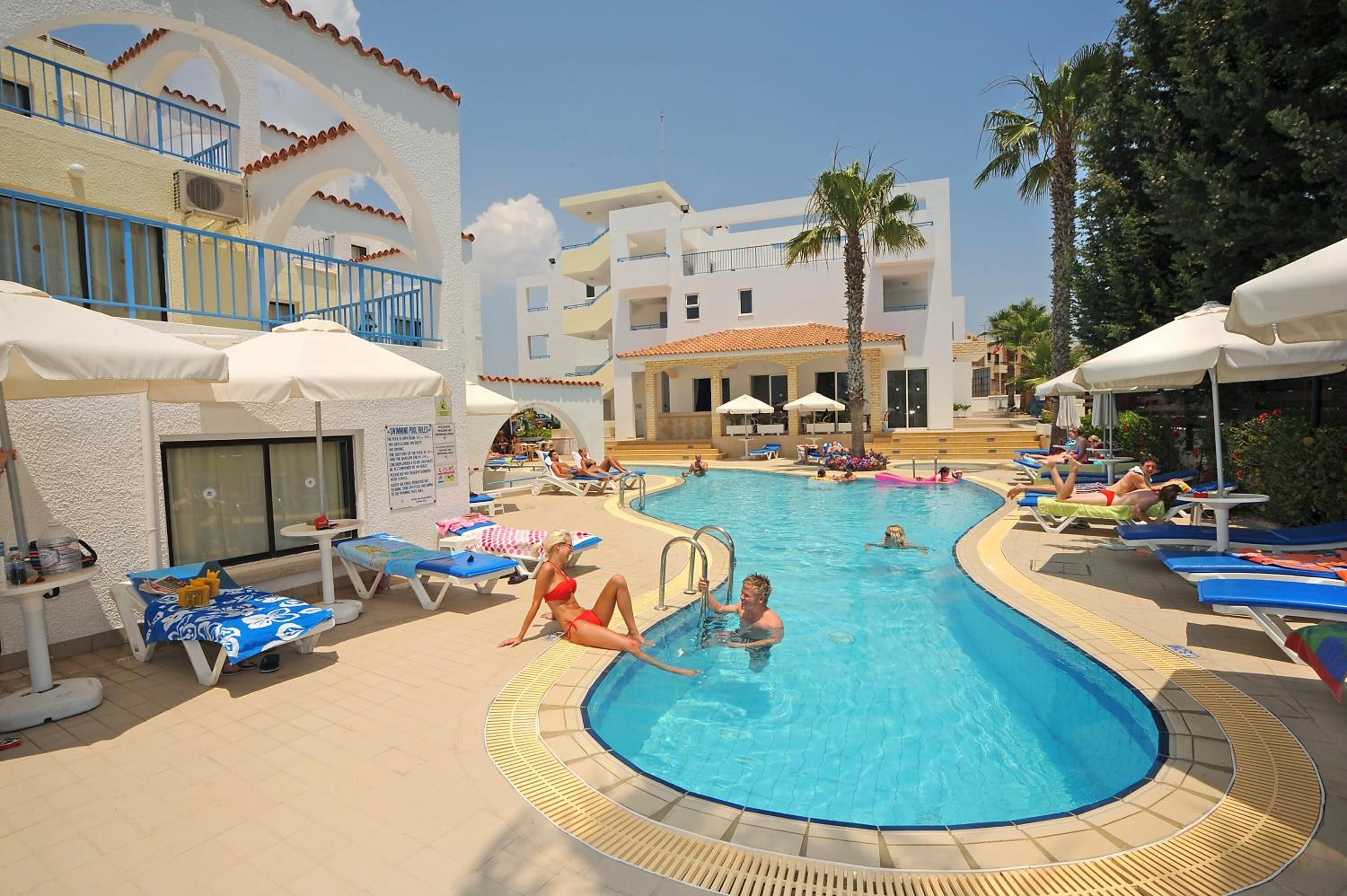 Un área de piscina con sillones de descanso, sombrillas y un edificio con balcones.
