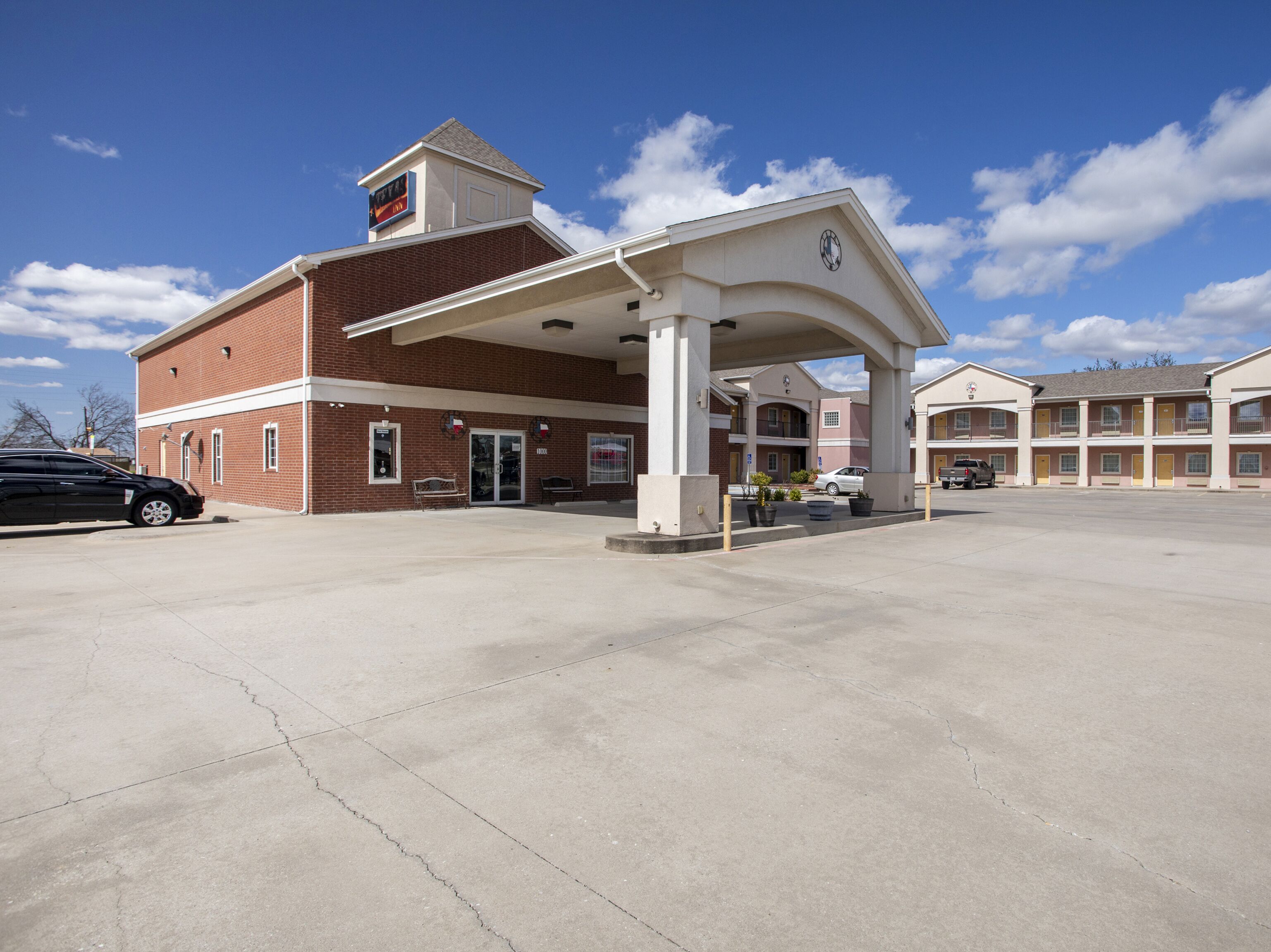 A motel with a covered parking area, multiple rooms, and a brick building.