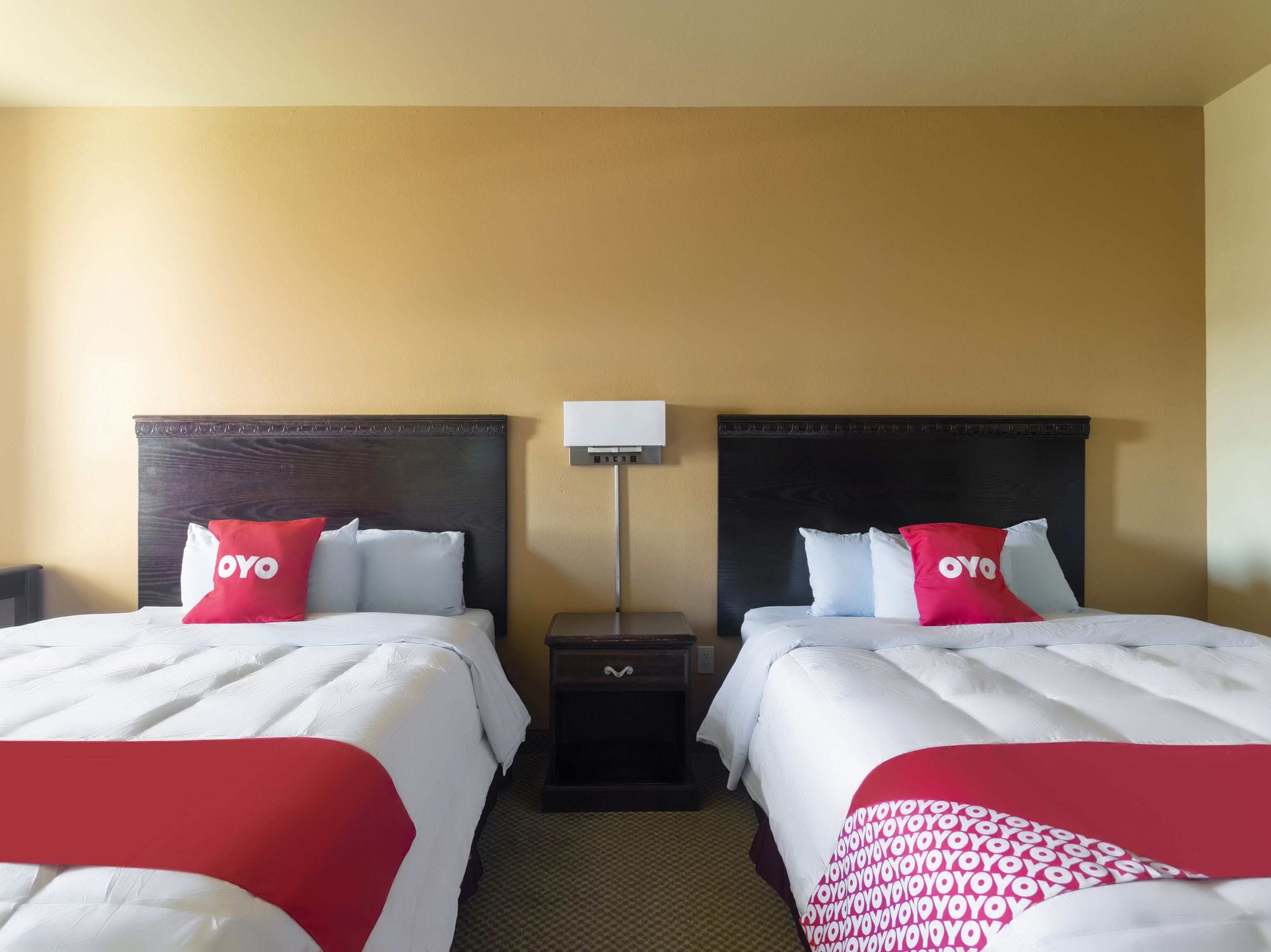 Ein Hotelzimmer mit zwei Betten, jedes mit einem roten und weißen Kopfkissen, einem Nachttisch und einer Lampe.