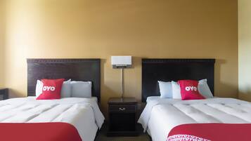 Ein Hotelzimmer mit zwei Betten, jedes mit einem roten und weißen Kopfkissen, einem Nachttisch und einer Lampe.