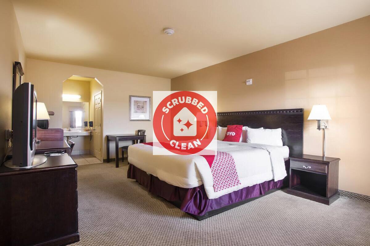 Una habitación de hotel con cama, mesita de noche, lámpara y televisor sobre un tocador.