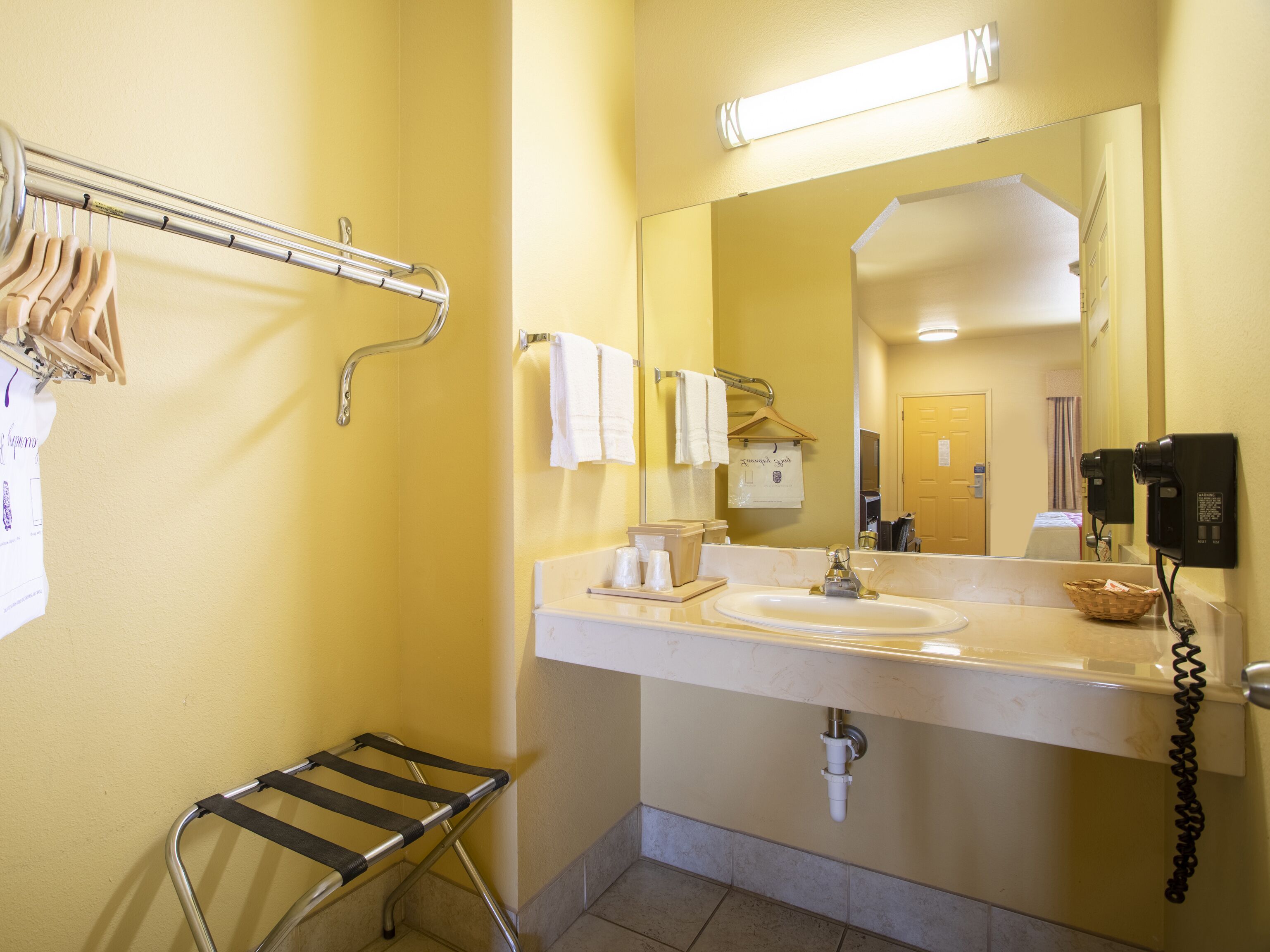 Un baño con lavamanos, espejo, toallero y secador de manos.