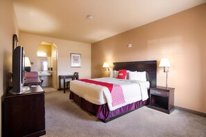 A hotel room with a bed, bedside tables, a desk, a television, and a bathroom visible through an open door.