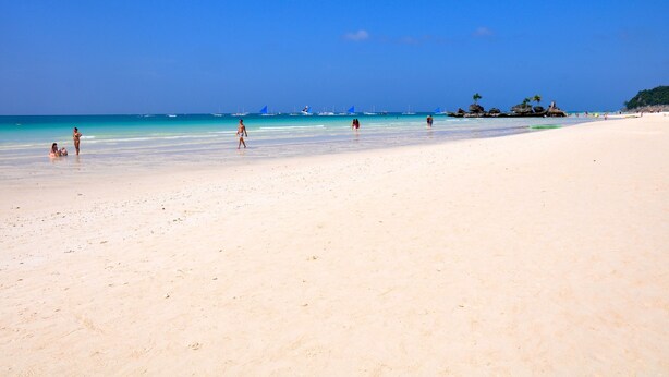 A wide sandy beach with clear blue water, a few people, and distant boats. - Boracay Beach Club (Boracay Island)