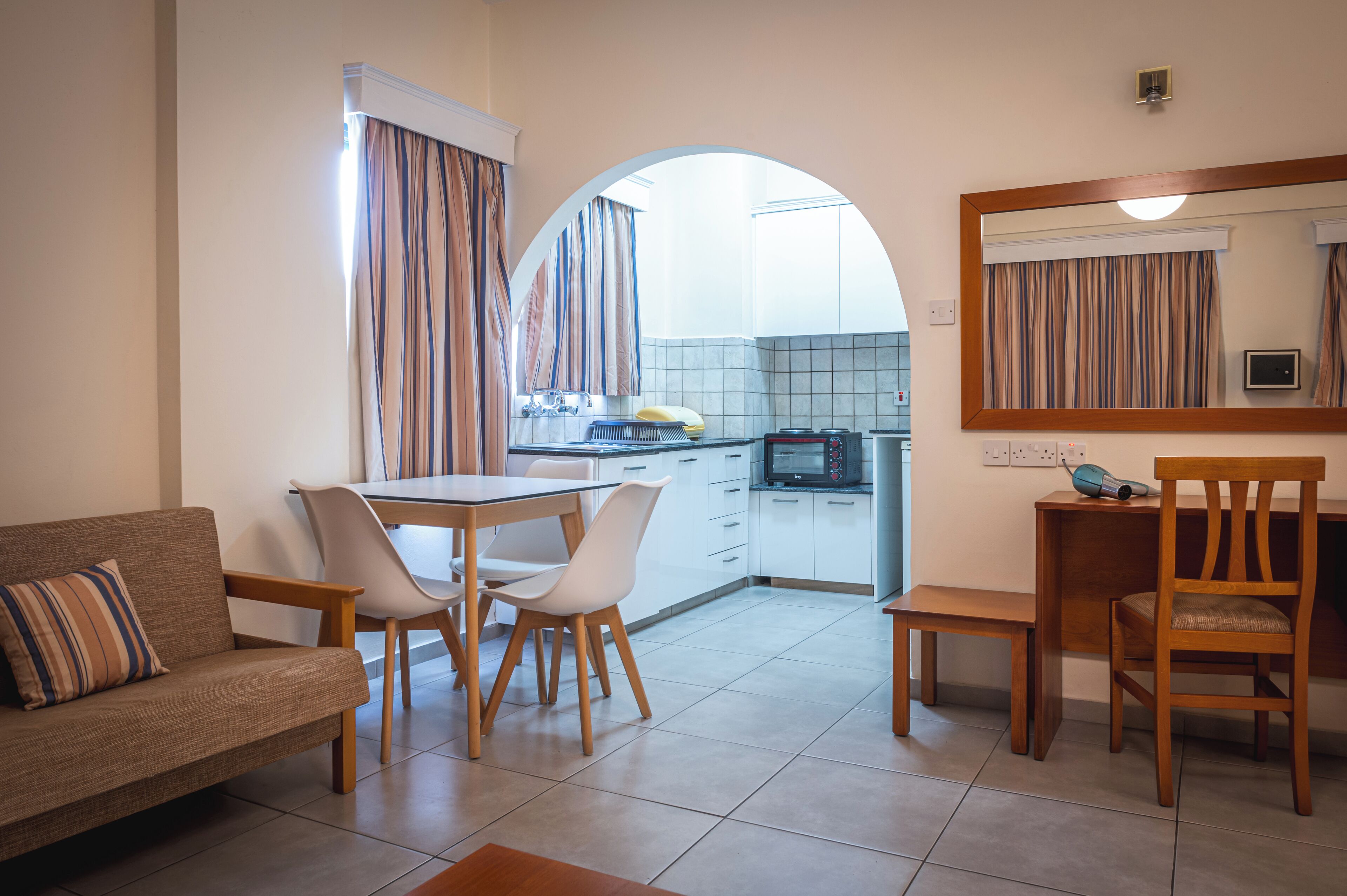 Un espace de vie compact comprenant un coin repas, une kitchenette et un canapé agrémenté d’un coussin à rayures.
