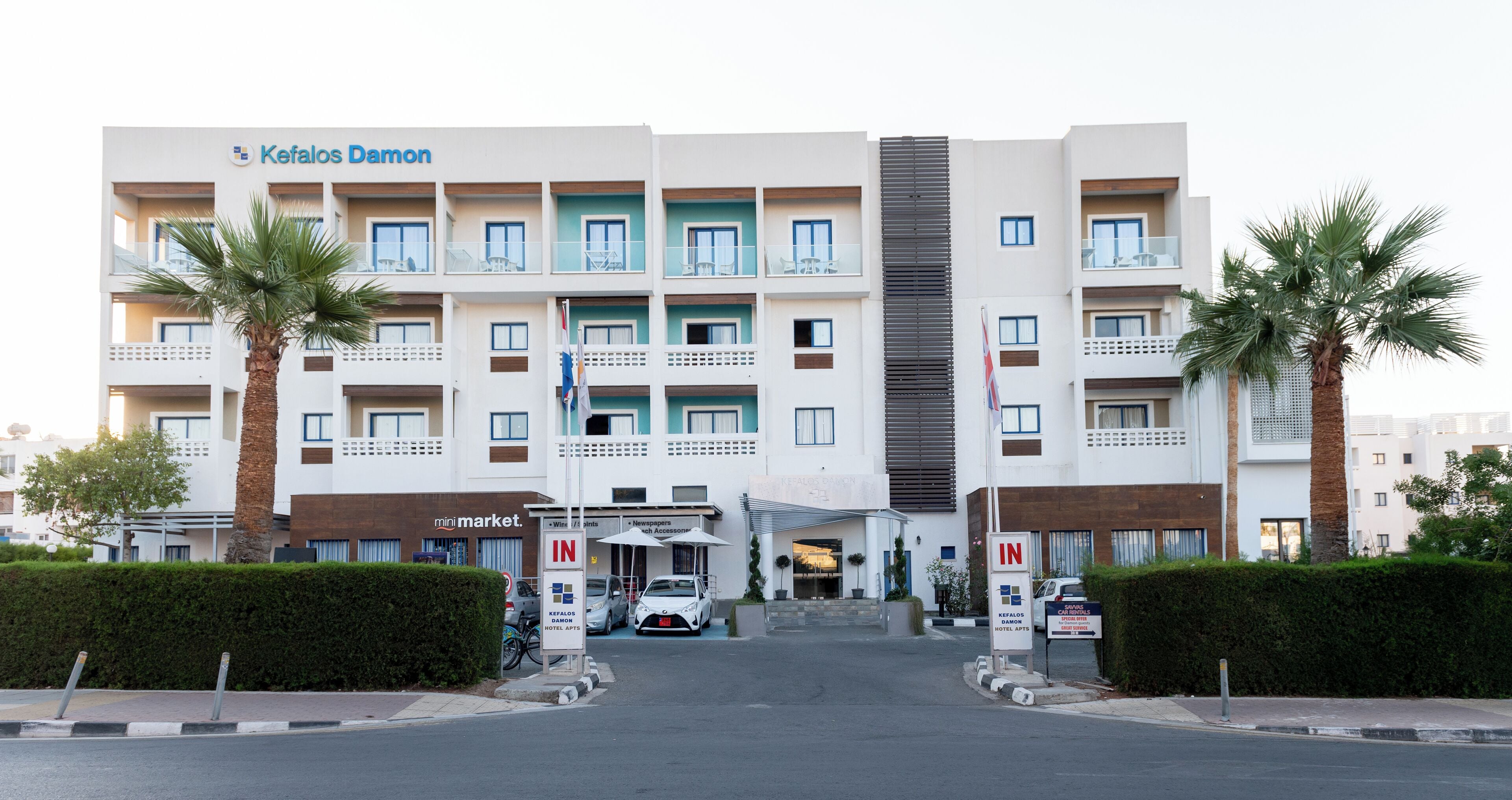 A multi-story hotel with a modern design, featuring balconies on each floor, a central entrance, and a sign indicating amenities like a mini market and hotel apps.