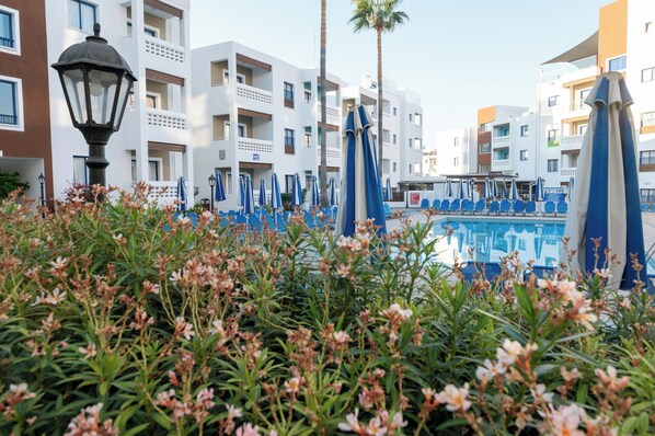A pool area with blue umbrellas, white buildings, and a lamp post.