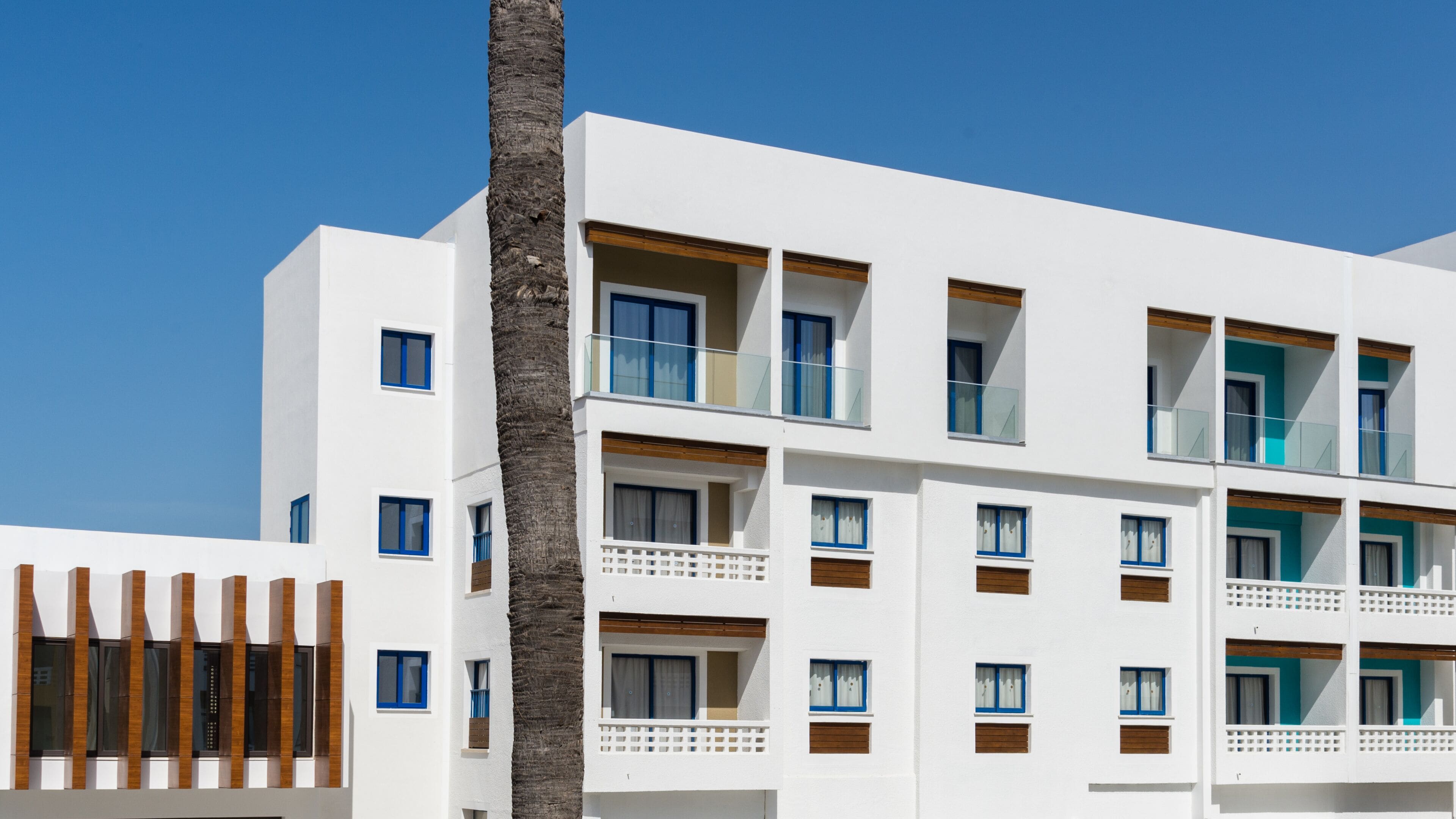 Un hotel moderno de varios pisos con paredes exteriores blancas, ventanas con marcos azules y detalles de madera.