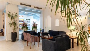 Ein modernes Wohnzimmer mit dunklen Sofas, einem gestreiften Sessel und einem Couchtisch. Große Kübelpflanzen und eine Lampe auf einem Beistelltisch sind ebenfalls vorhanden.